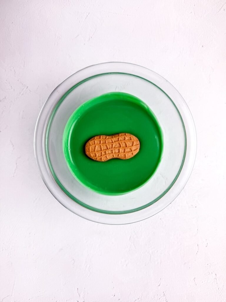 Cookie being dipped into a bowl of melted green candy coating to make cookies.