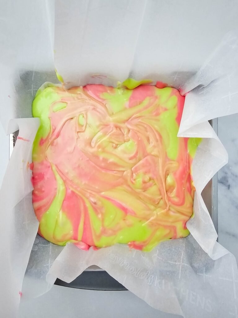 Red, green, and white melted fudge swirled together in a parchment-lined baking pan to create festive dessert.