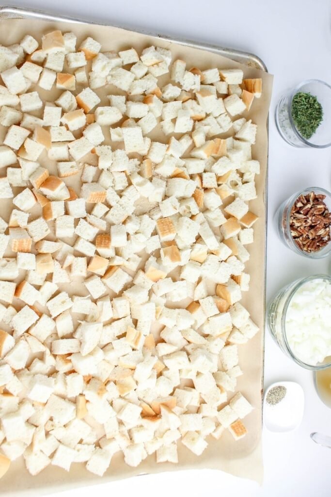 Cubes of bread spread on a baking sheet lined with parchment paper, ready to be toasted.