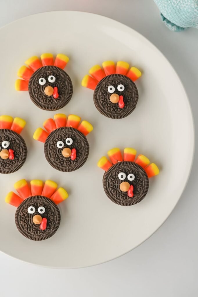 Top view of Turkey Oreo Cookies decorated with candy corn feathers, candy eyes, and frosting wattles arranged on a white plate.