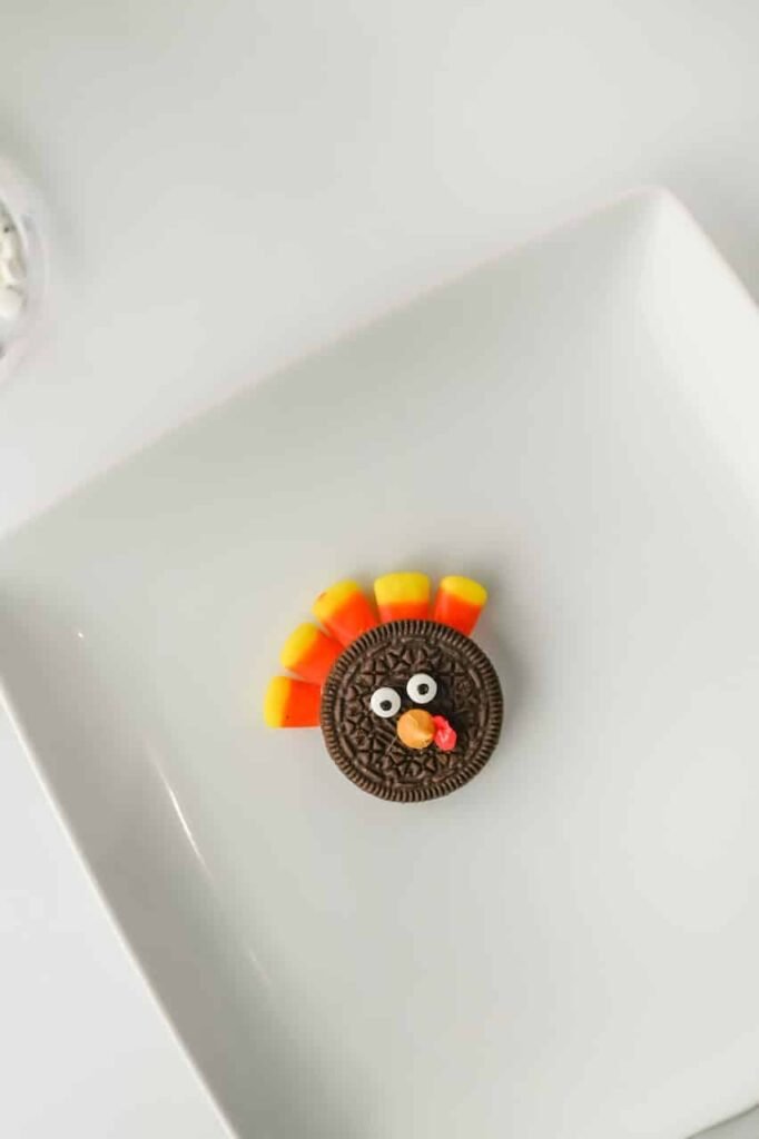 Completed Thanksgiving treats decorated with candy corn feathers, candy eyes, butterscotch chip beak, and red frosting wattle on a white plate.