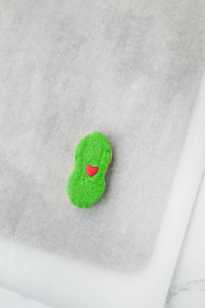 Green candy-coated treats topped with a single red heart sprinkle.