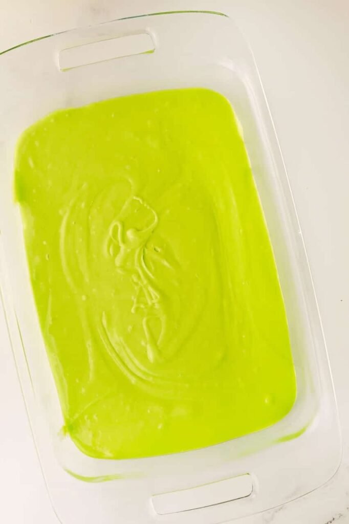 Bright green cake batter poured evenly into a glass baking dish, ready to bake for a festive Grinch poke cake.