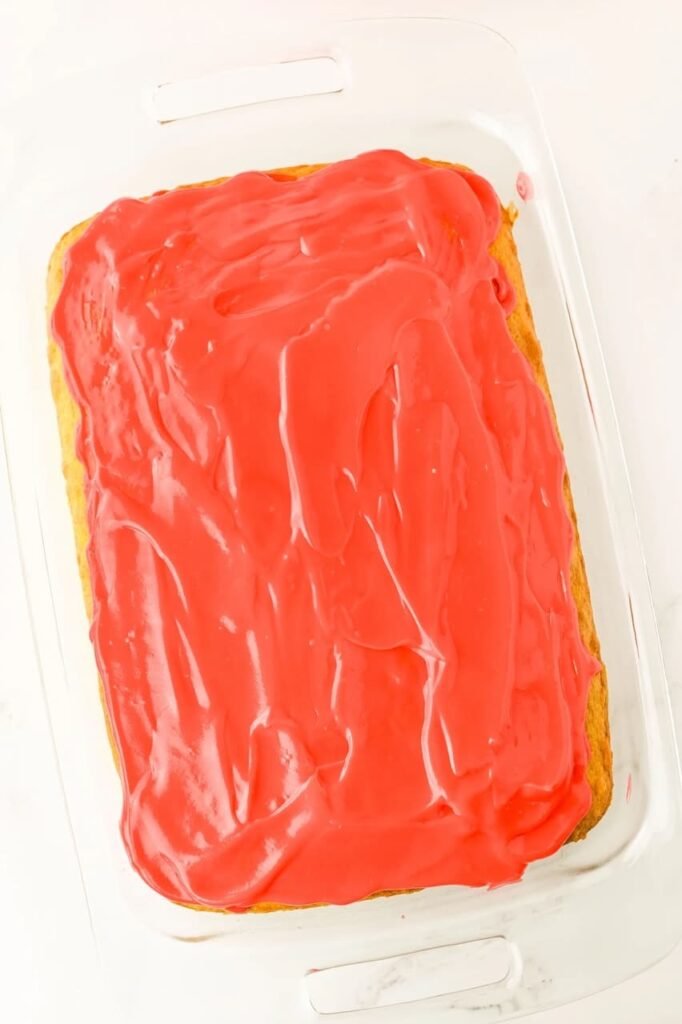 cake in a glass pan topped with a smooth layer of red cheesecake pudding filling, ready to chill before frosting.