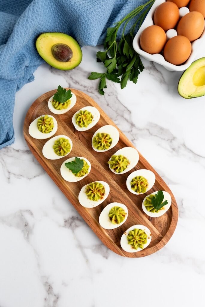 Overhead shot of avocado deviled eggs on a wooden platter, a healthy no-mayo appetizer made with ripe avocados and hard-boiled eggs.