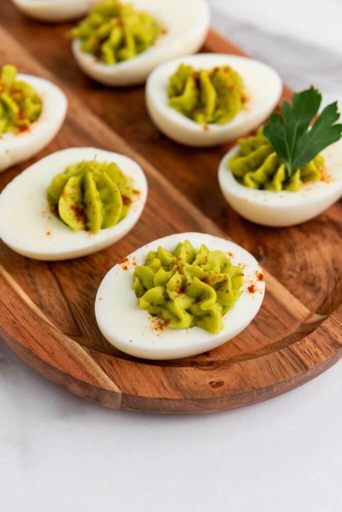 Close-up of creamy avocado deviled eggs on a wooden platter, a healthy no-mayo appetizer topped with paprika and parsley.
