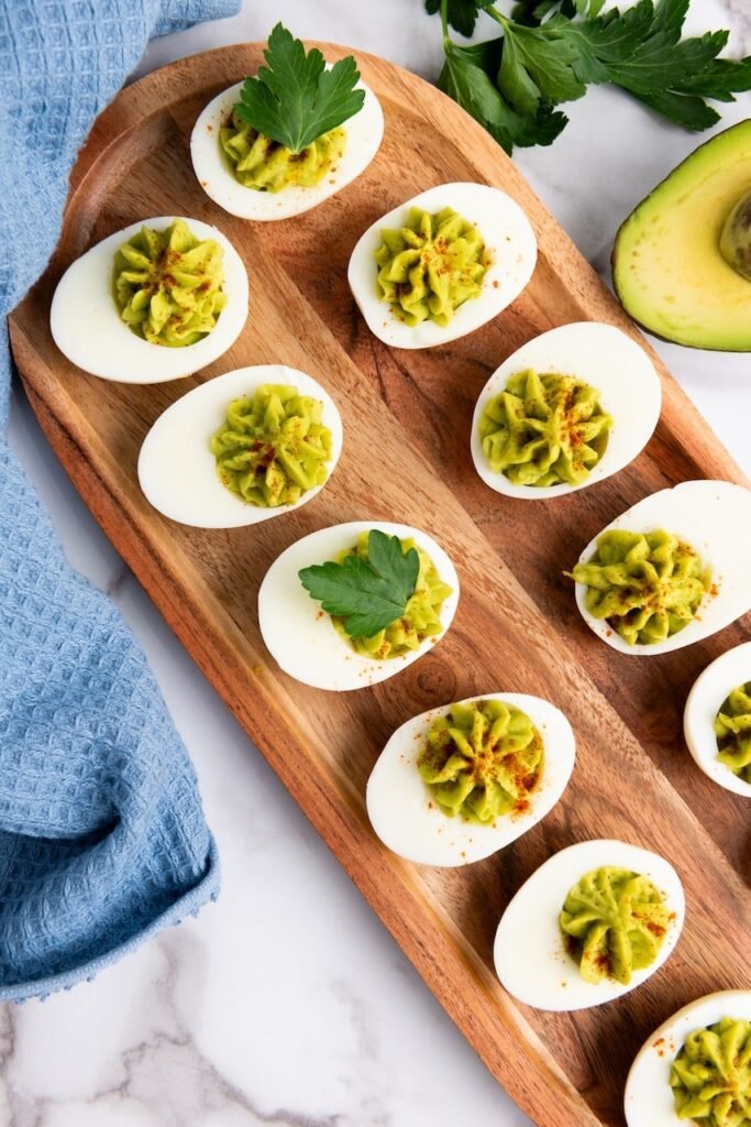 Close-up overhead view of avocado deviled eggs on a wooden platter, a healthy no-mayo appetizer garnished with paprika and parsley.