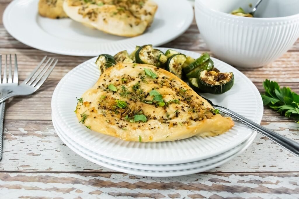 Juicy broiled chicken breast served with roasted zucchini and fresh herbs on a white plate — a simple, healthy dinner idea.