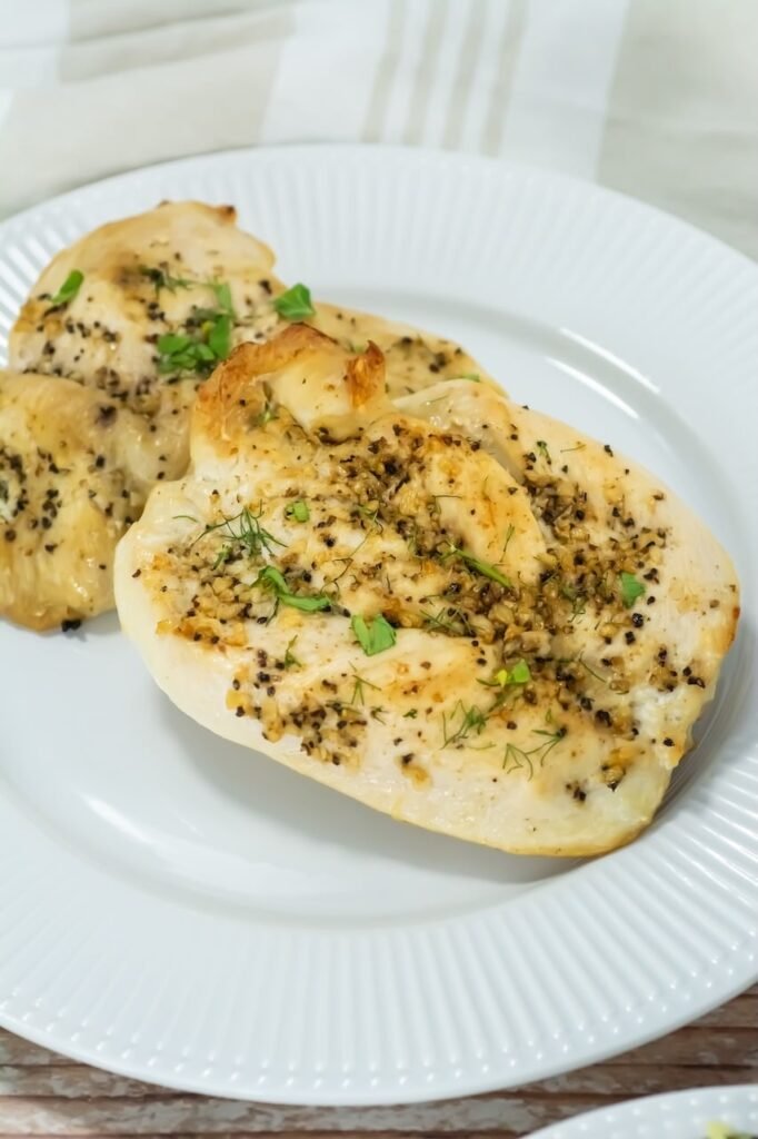 Juicy broiled chicken breasts garnished with fresh parsley and dill on a white plate, showing golden edges and garlic herb seasoning.