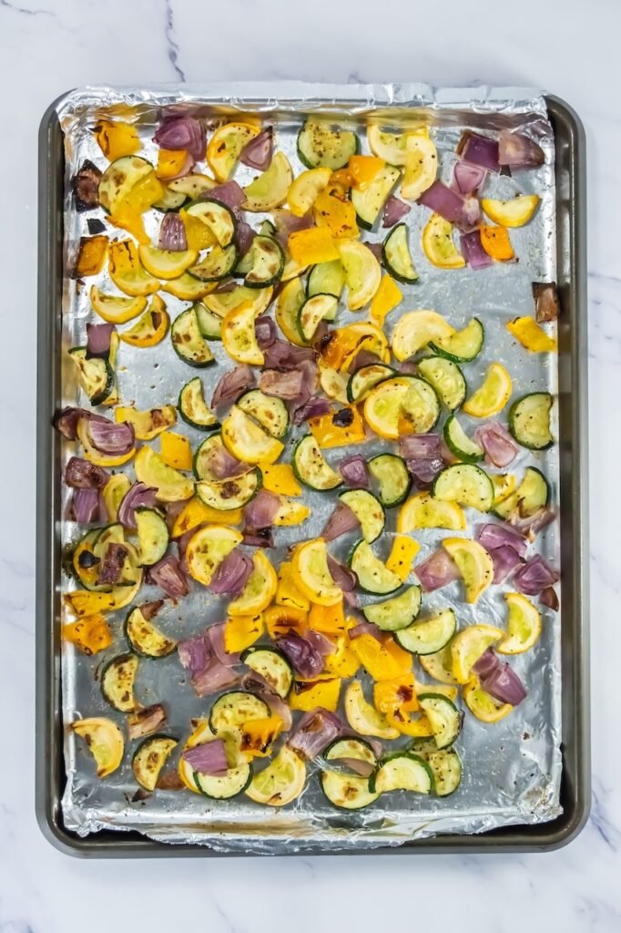 Broiled zucchini, yellow squash, red onion, and bell pepper with caramelized edges on a foil-lined baking sheet.