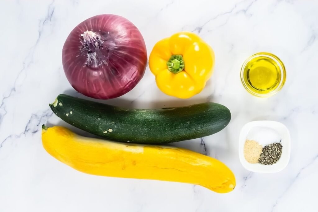 Fresh zucchini, yellow squash, red onion, and yellow bell pepper with olive oil and seasonings for broiled vegetables.