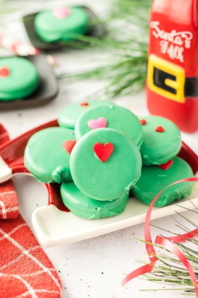 Stack of green Grinch Oreos with red and pink heart sprinkles on a festive tray beside Santa’s milk bottle.
