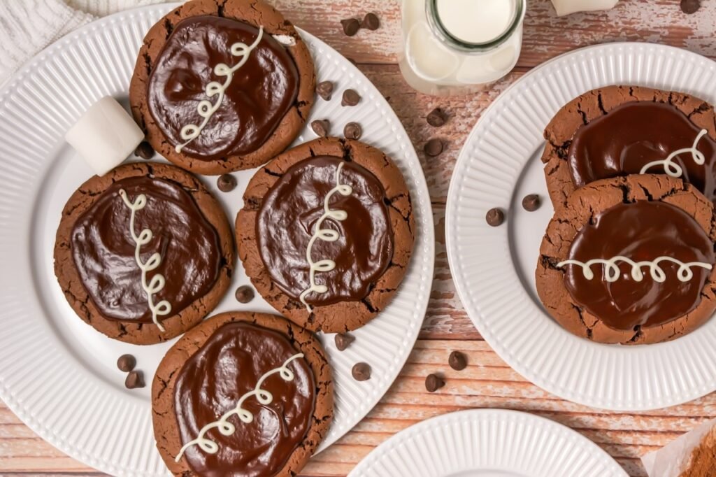 Overhead view of crumbl chocolate mallow cupcake cookies topped with chocolate ganache and white chocolate drizzle served on plates with milk.