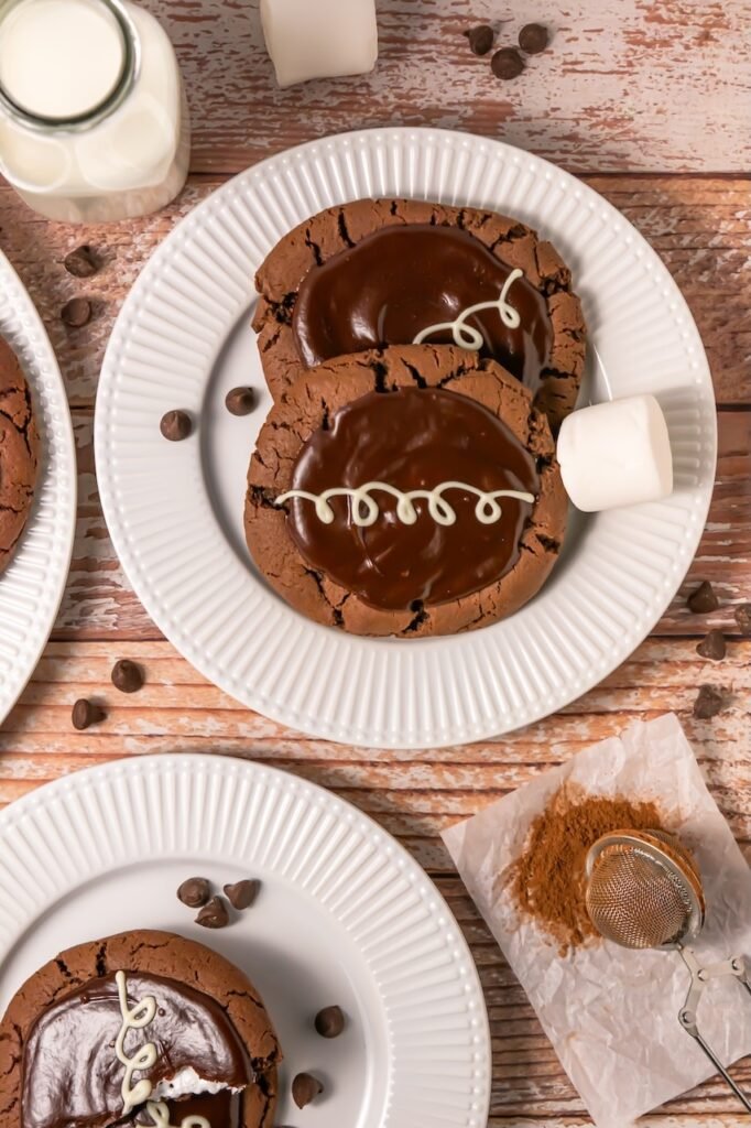 Crumbl chocolate mallow cupcake cookies topped with ganache and white chocolate drizzle served on plates with marshmallows and milk.