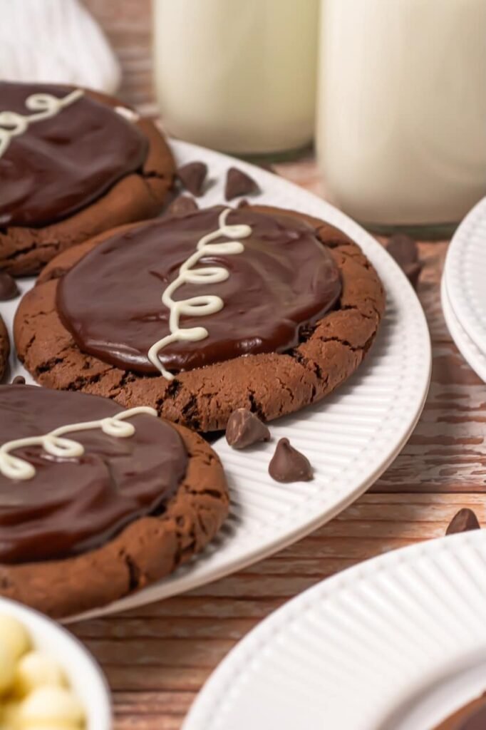 Plate of crumbl chocolate mallow cupcake cookies topped with chocolate ganache and white chocolate drizzle served with milk and chocolate chips.