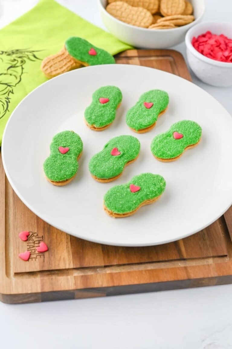 Plate of Grinch Nutter Butter cookies with green sugar coating and red heart sprinkles, a fun no-bake Christmas cookie recipe.