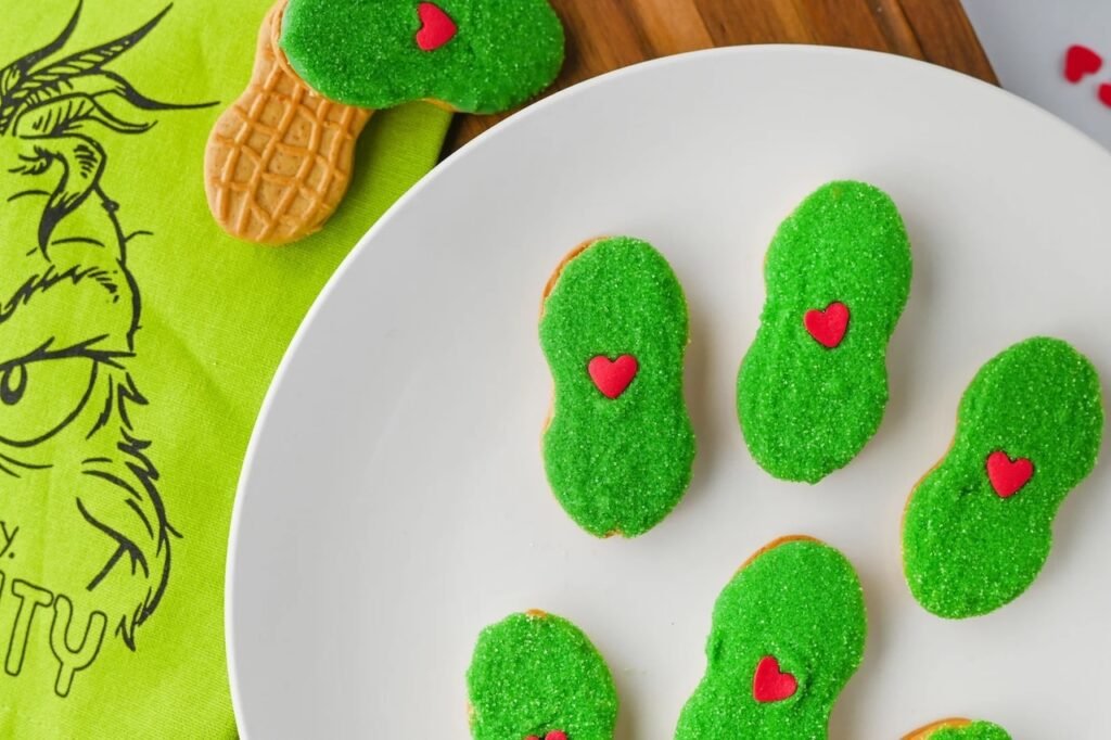 Plate of Grinch Nutter Butter cookies with green sanding sugar and red hearts, a fun no bake Christmas dessert for kids.