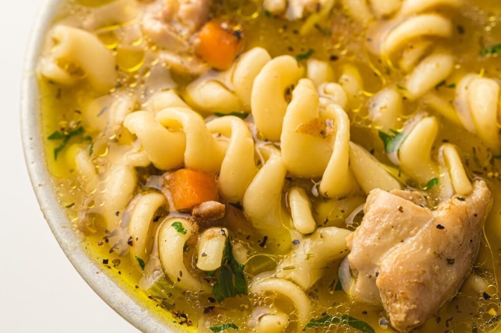 Close-up of homemade chicken noodle soup with spiral noodles, tender chicken pieces, carrots, and herbs floating in a rich, brothy soup.