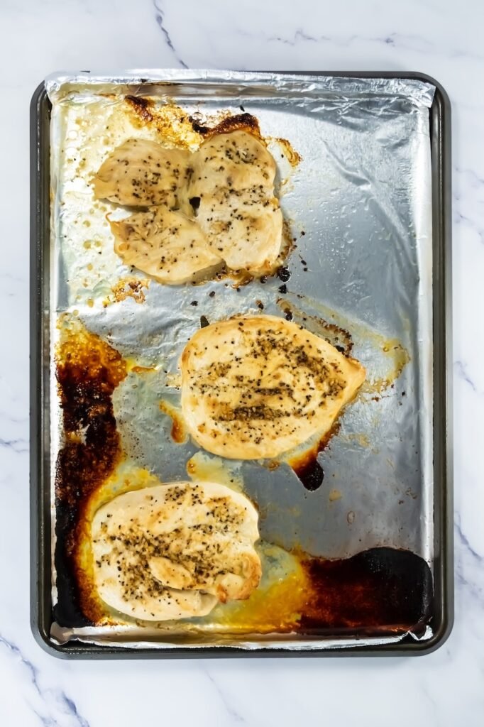 Step 5 in recipe – cooked chicken breasts with golden edges on a foil-lined baking sheet right after broiling.