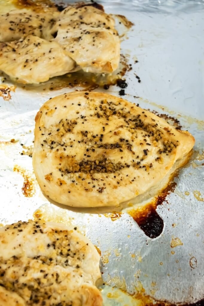 Step 6 in broiled chicken recipe – close-up of chicken breasts after flipping, starting to brown with garlic and pepper seasoning.