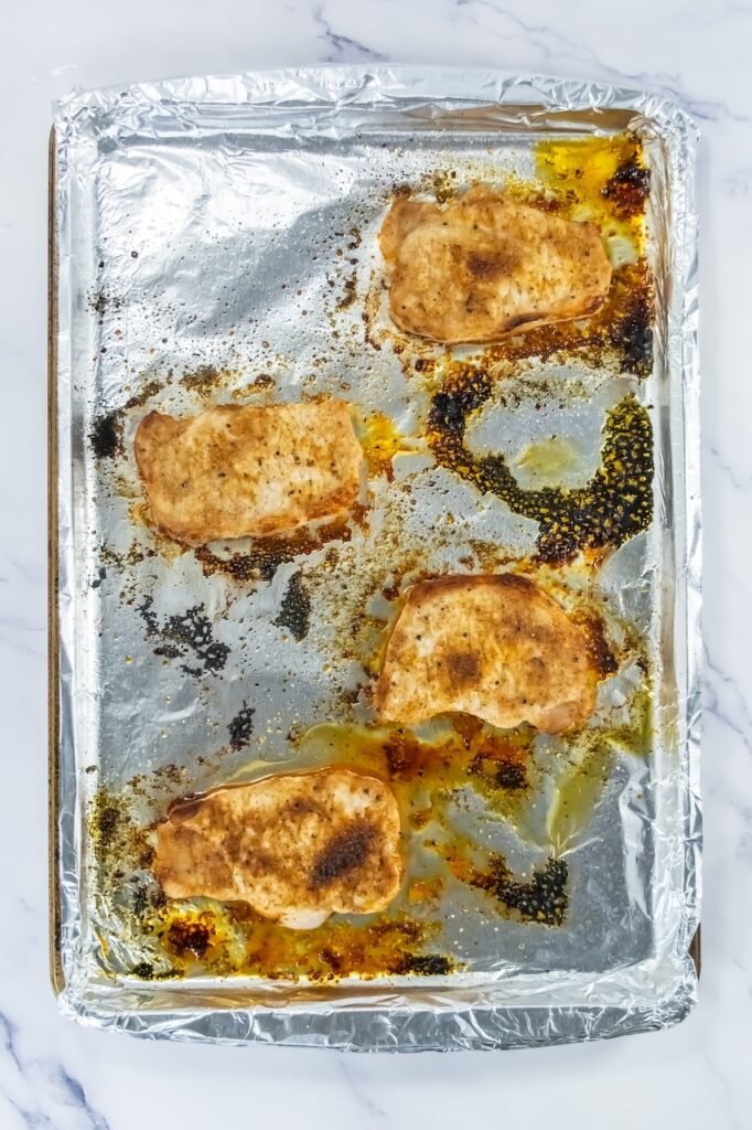 Golden-brown broiled pork chops on a foil-lined baking sheet just out of the oven.