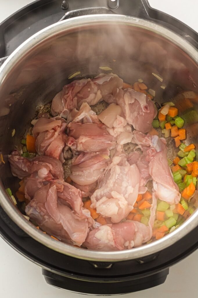 Raw sliced chicken thighs added to sautéed carrots, celery, and onions inside the Pot while preparing the soup.