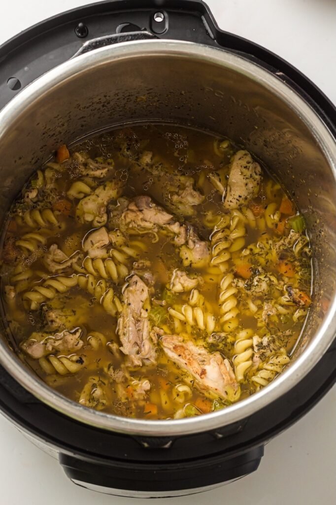 Fully cooked food inside the Pot, with tender chicken pieces, pasta, carrots, celery, and herbs in a hot broth.