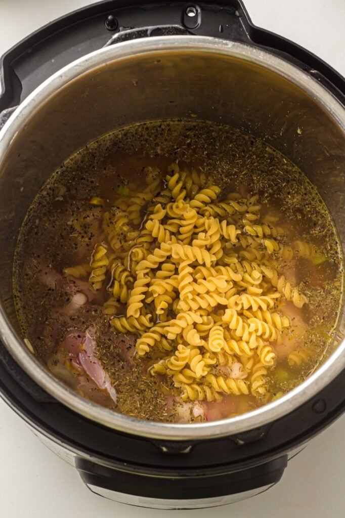 Uncooked fusilli pasta added to the pot filled with chicken, broth, and seasonings while preparing the recipe.