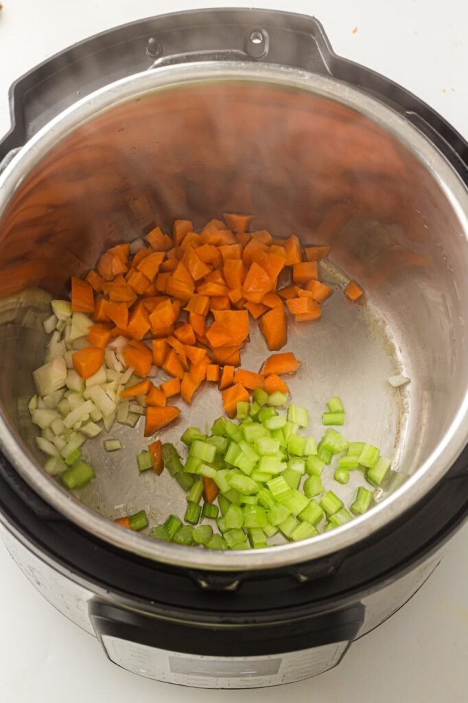Chopped carrots, celery, and onions sautéing inside an Instant Pot during the first step of making the recipe.