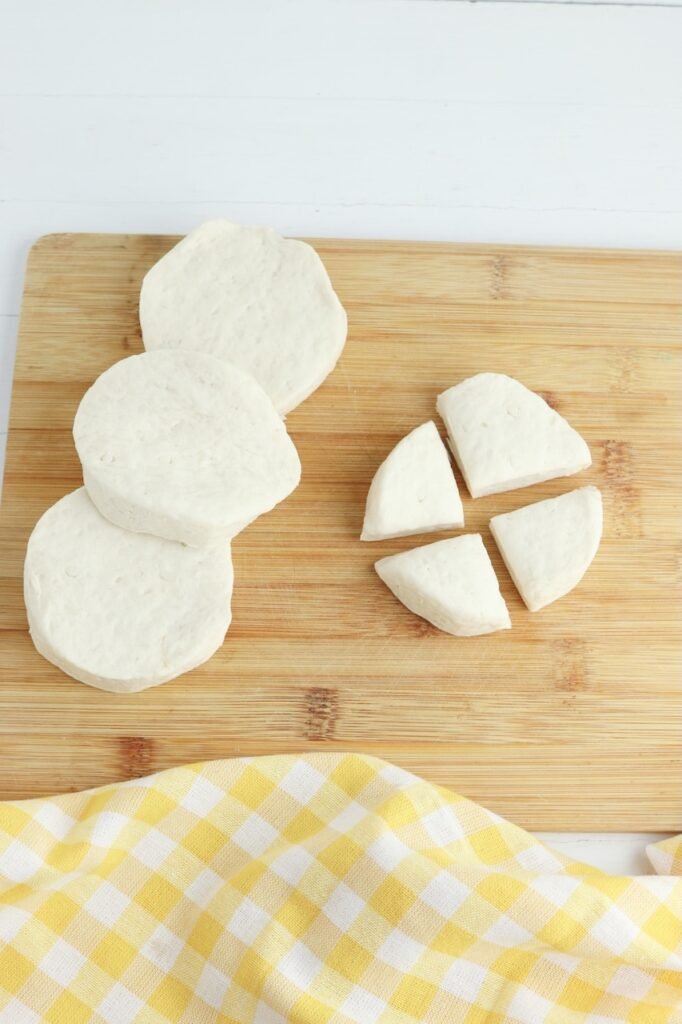 Canned biscuit dough rounds on a cutting board with one cut into quarters.