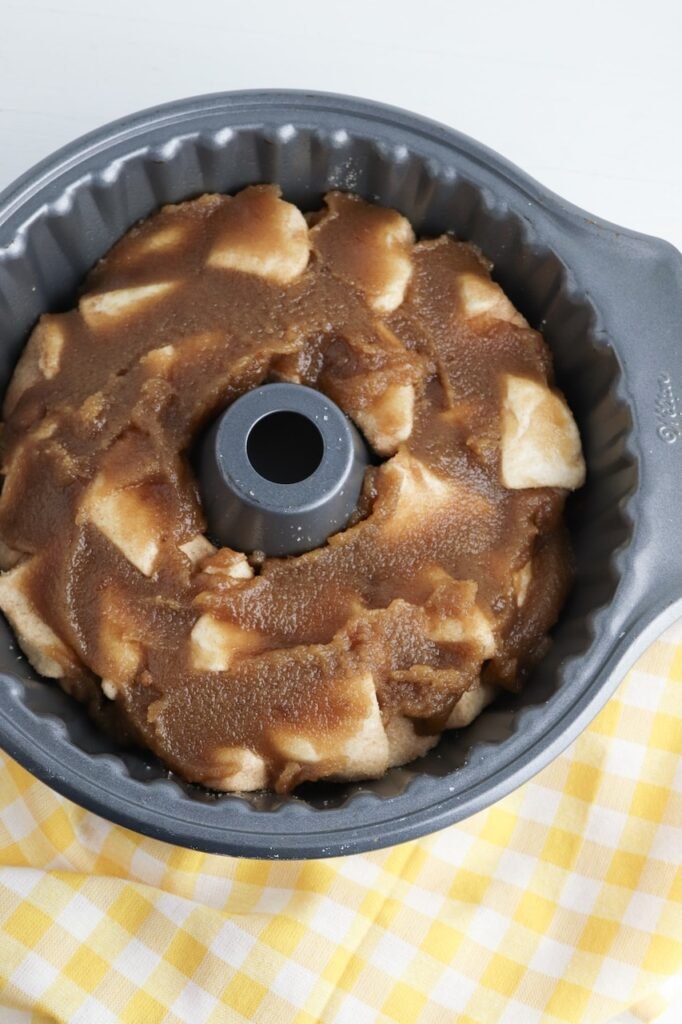 Biscuit dough pieces in a Bundt pan covered with brown sugar and melted butter mixture before baking.