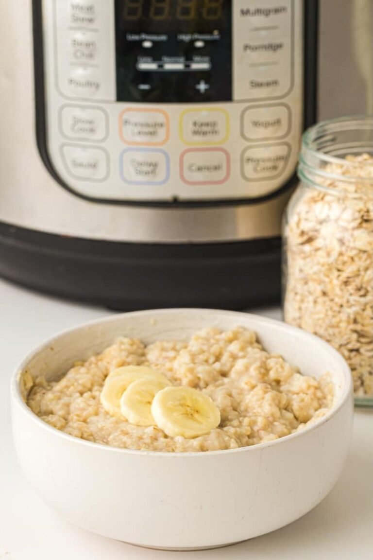A bowl of creamy cooked oatmeal topped with sliced banana sitting in front of an Instant Pot, showing a finished serving of oatmeal ready for breakfast.