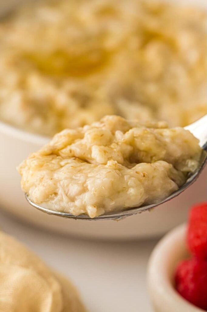 A spoon holding a thick, creamy scoop of cooked oatmeal in front of a bowl, showing the smooth texture and fully softened oats after cooking in the Instant Pot.