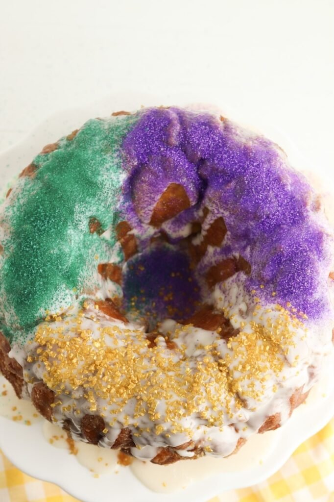 Top view of pull apart King Cake decorated with purple, green, and gold sprinkles on vanilla glaze