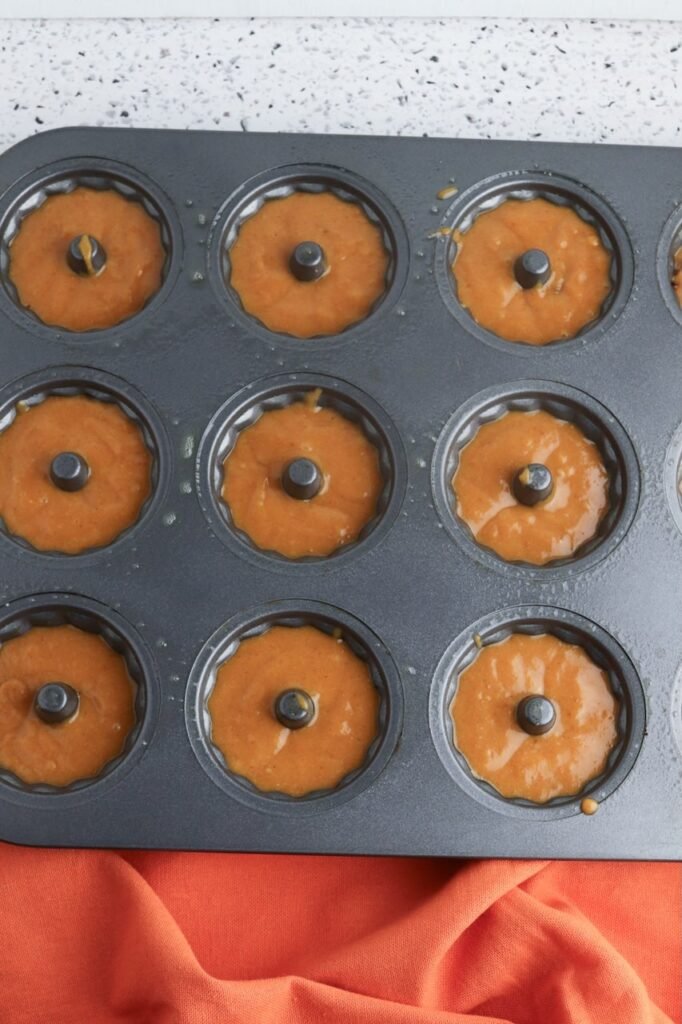A dark nonstick mini Bundt pan filled with pumpkin cake batter portioned evenly into each cavity, ready to be baked in the oven.
