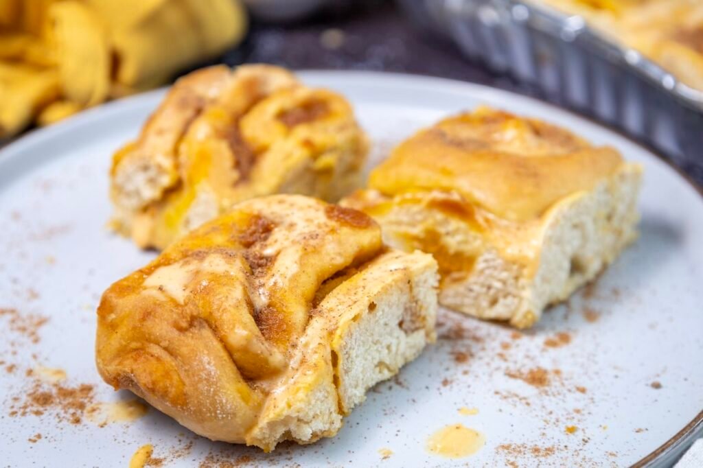 Soft pumpkin cinnamon rolls with cream cheese frosting served on a plate, showing the fluffy interior, cinnamon swirl, and tender crumb texture.