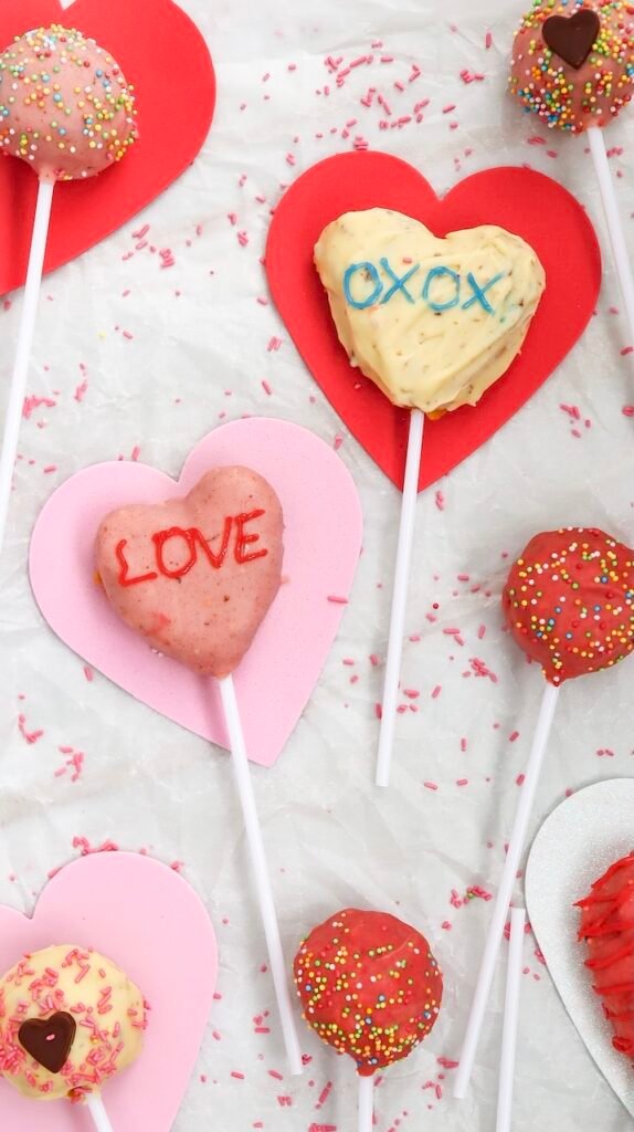 Overhead view of heart-shaped pink and white treats decorated with sprinkles and handwritten messages, a festive dessert idea for Valentine parties and homemade edible gifts.