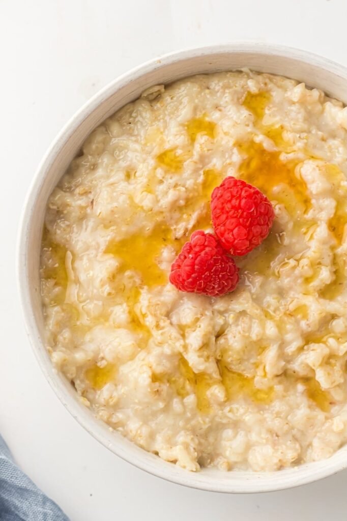 A bowl of creamy cooked oatmeal topped with fresh raspberries and a light drizzle, showing a finished serving of Instant Pot oatmeal ready to eat.