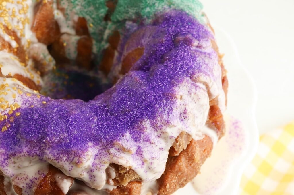Close-up of pull apart King Cake with vanilla glaze and purple sugar sprinkles highlighting the texture of the baked dough