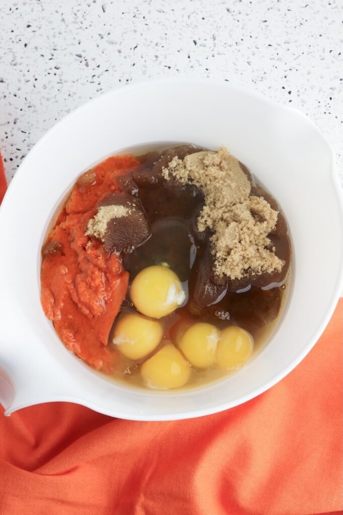 A white mixing bowl filled with pumpkin purée, eggs, brown sugar, oil, and vanilla before being stirred together to make the wet batter for pumpkin mini Bundt cakes.