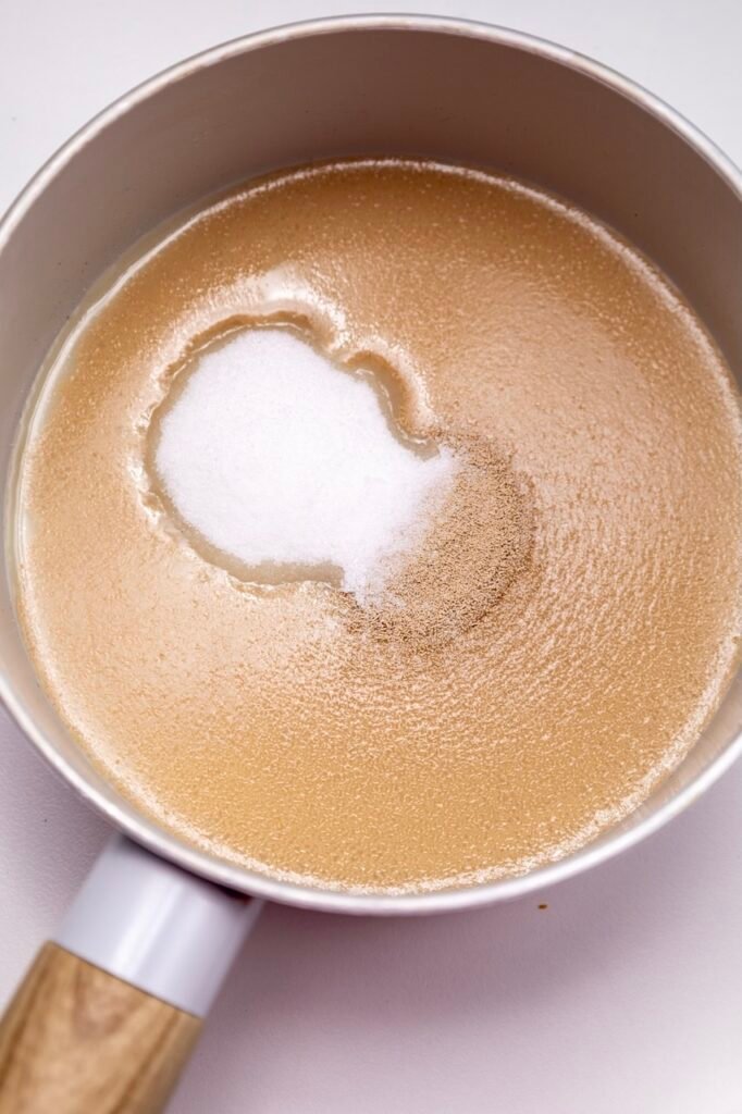 Warm milk mixed with yeast and sugar in a saucepan, showing the yeast beginning to dissolve and bloom before making.