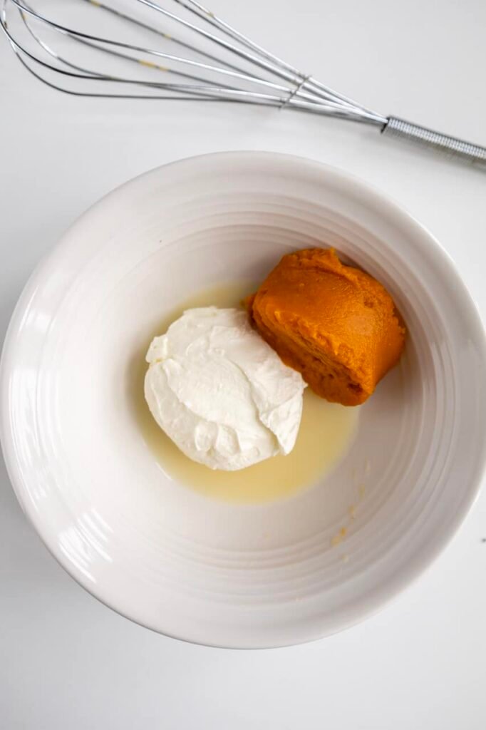 Softened cream cheese and pumpkin purée in a bowl with liquid, ready to be whisked into pumpkin cream cheese frosting for cinnamon rolls.