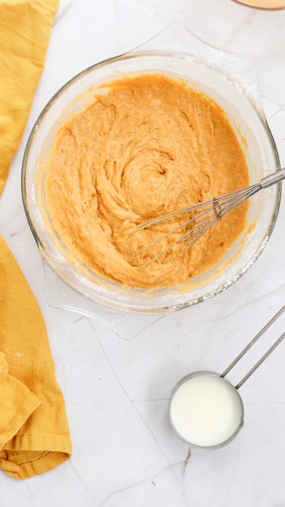 Overhead view of a glass mixing bowl filled with smooth pumpkin pancake batter, showing the wet and dry ingredients fully combined and ready to be poured onto a skillet for cooking.