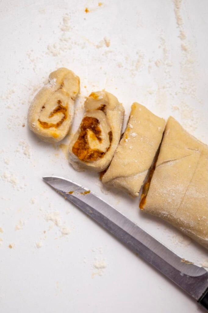 Sliced dough on a lightly floured surface, showing the spiral filling and a knife used to cut the rolls before baking.