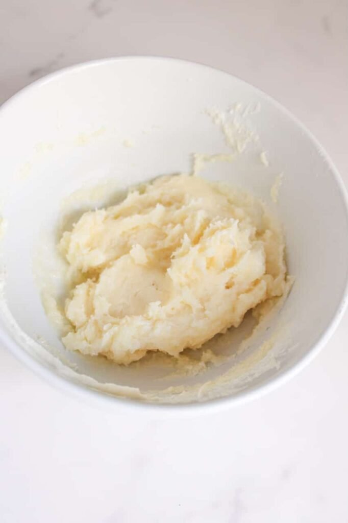 A white mixing bowl filled with a thick, creamy blend of melted white chocolate and cream cheese. The mixture is smooth, slightly glossy, and ready to be scooped into a piping bag for assembling.