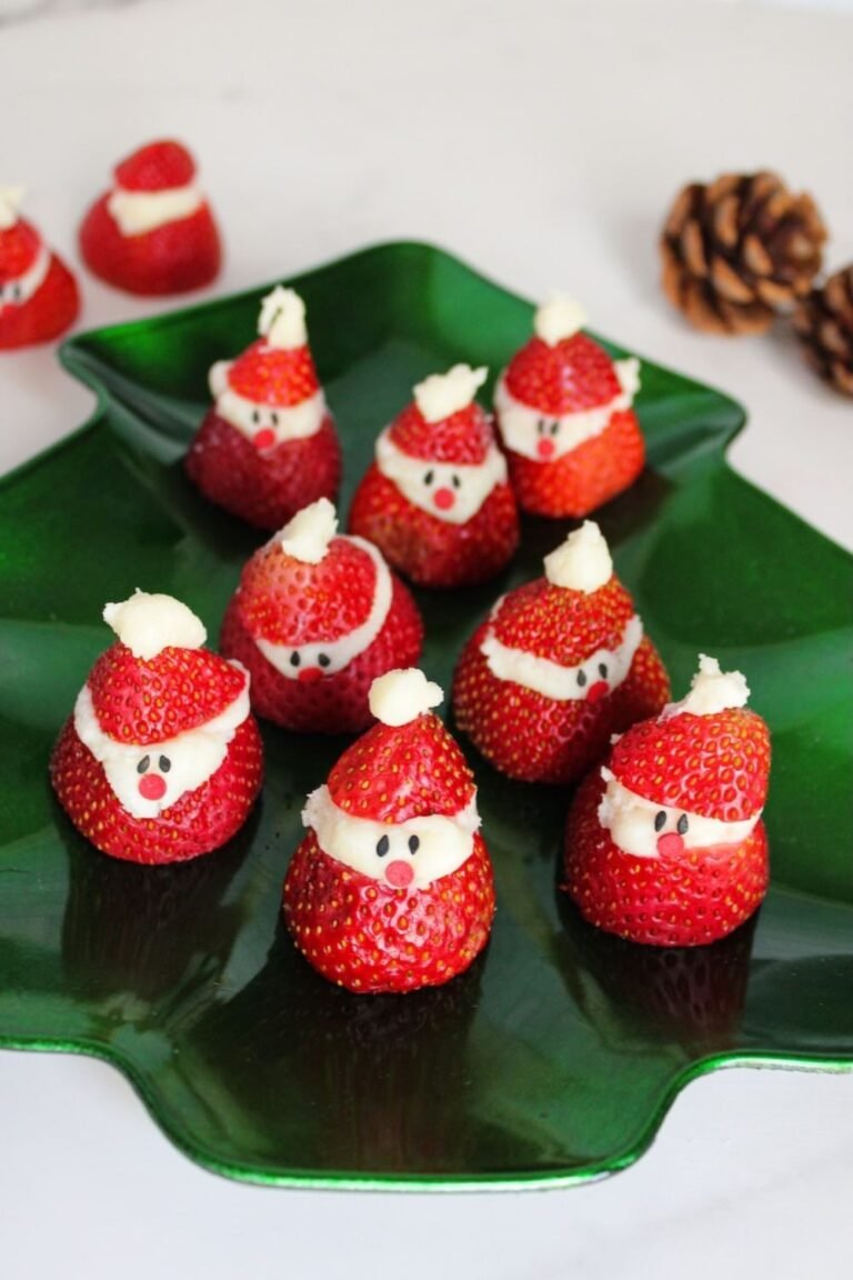 Strawberry Santas arranged on a green Christmas-tree-shaped platter, each with a white chocolate cream cheese filling and sprinkle eyes and nose.