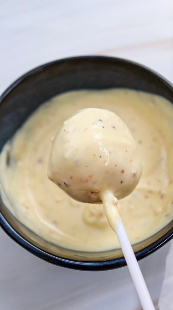 Close-up of a cake pop freshly dipped in melted white chocolate, showing a smooth coating during the decorating step for Valentine’s Day cake pops.