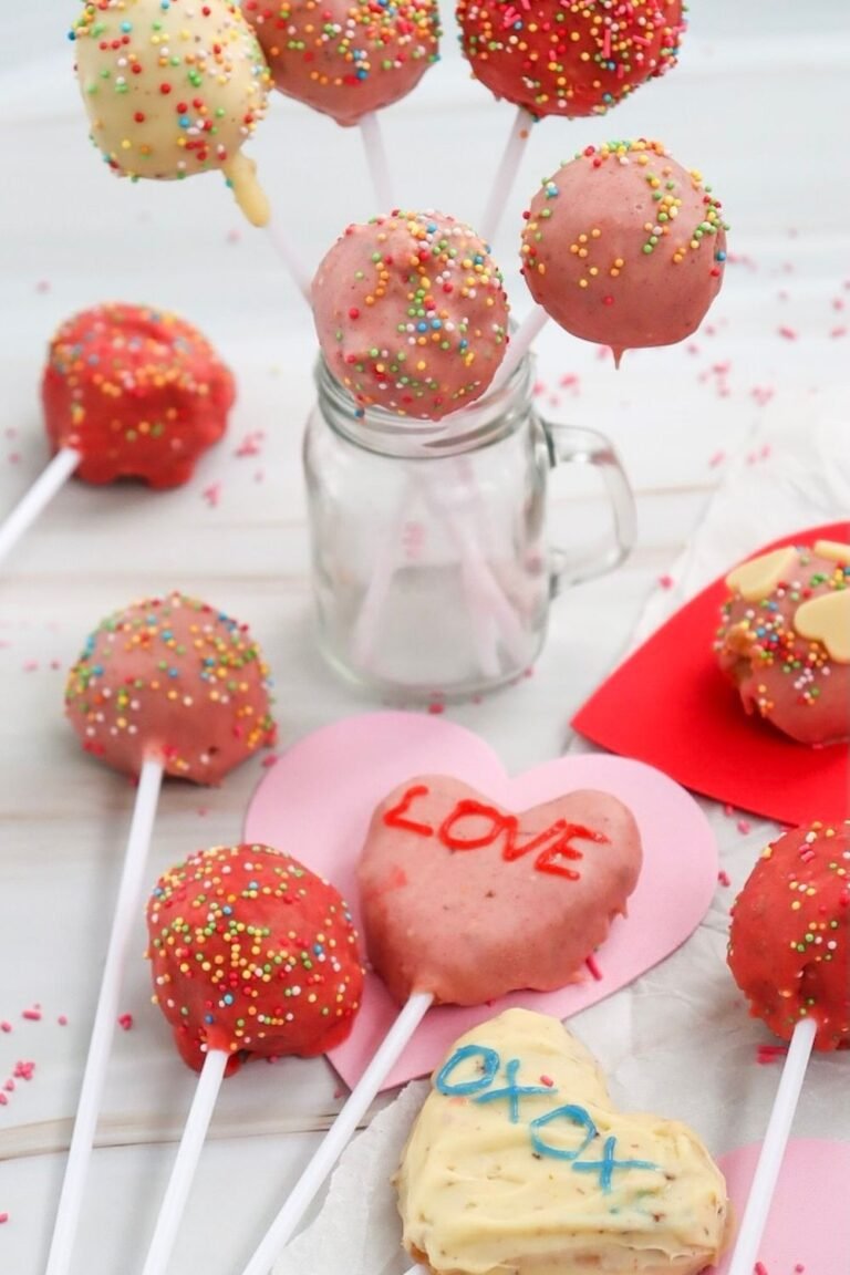 Bright Valentine’s Day cake pops decorated with sprinkles, pink and white chocolate, and heart-shaped pops with LOVE and XOXO messages displayed in a jar and on heart cutouts.