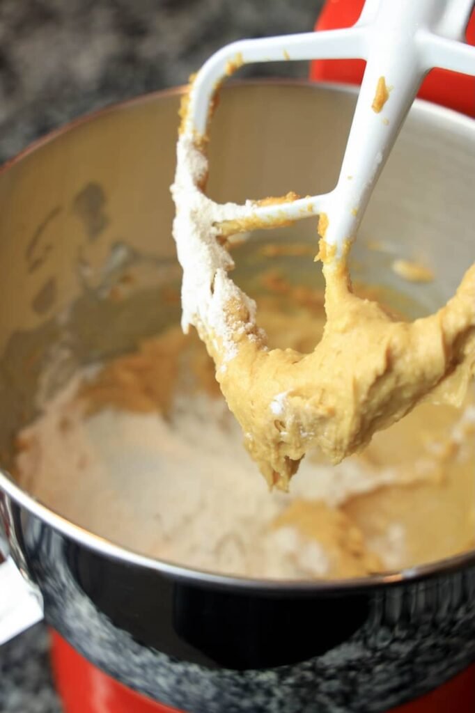 Flour being mixed into peanut butter cookie dough in a stand mixer bowl, showing the dough as it thickens while dry ingredients are incorporated for Valentine’s M&M cookies.