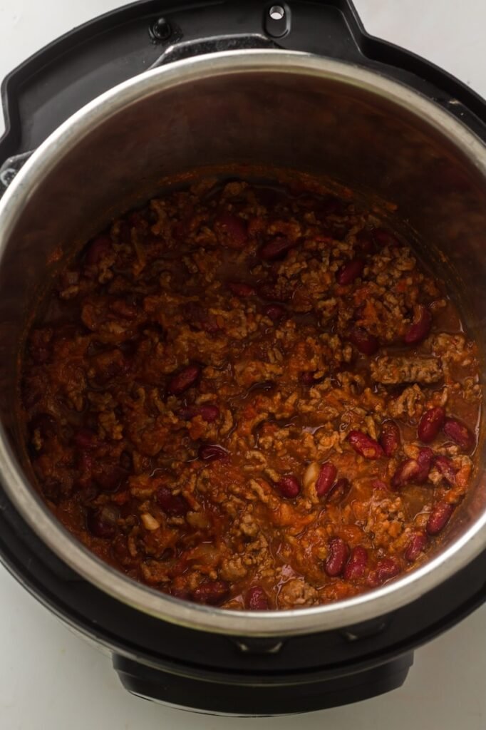 Fully cooked Instant Pot chili inside the inner pot, showing thick chili with browned ground beef, kidney beans, and tomatoes after pressure cooking and resting, ready to be stirred and served.